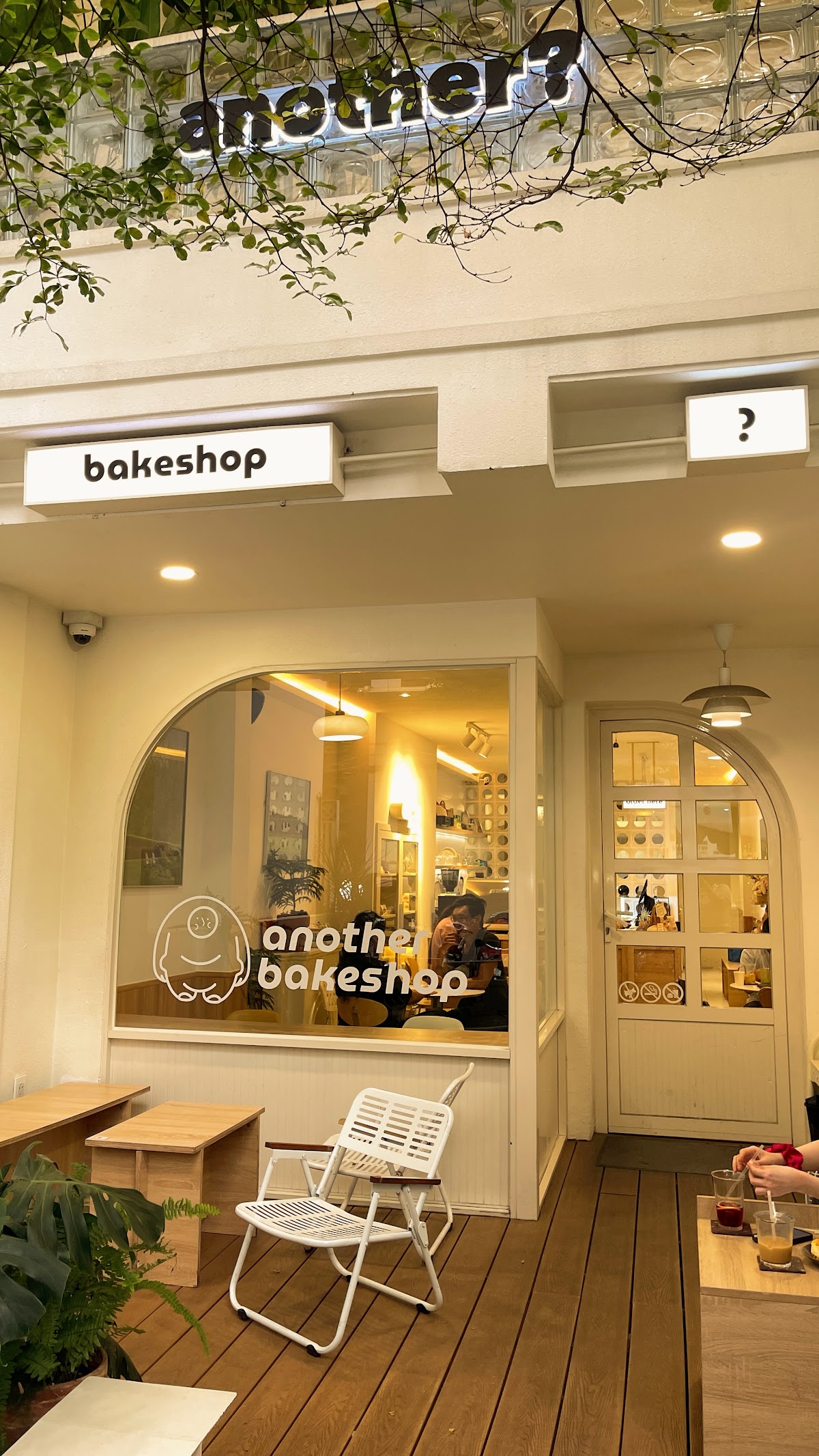 외관 — 백라이트 “bakeshop” 간판, 검은 “another?” 글자, 아치 로고 창
