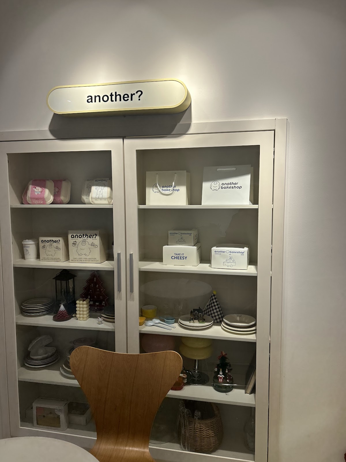 실내 — 흰 진열장, 불 켜진 “another?” 간판, 브랜드 포장