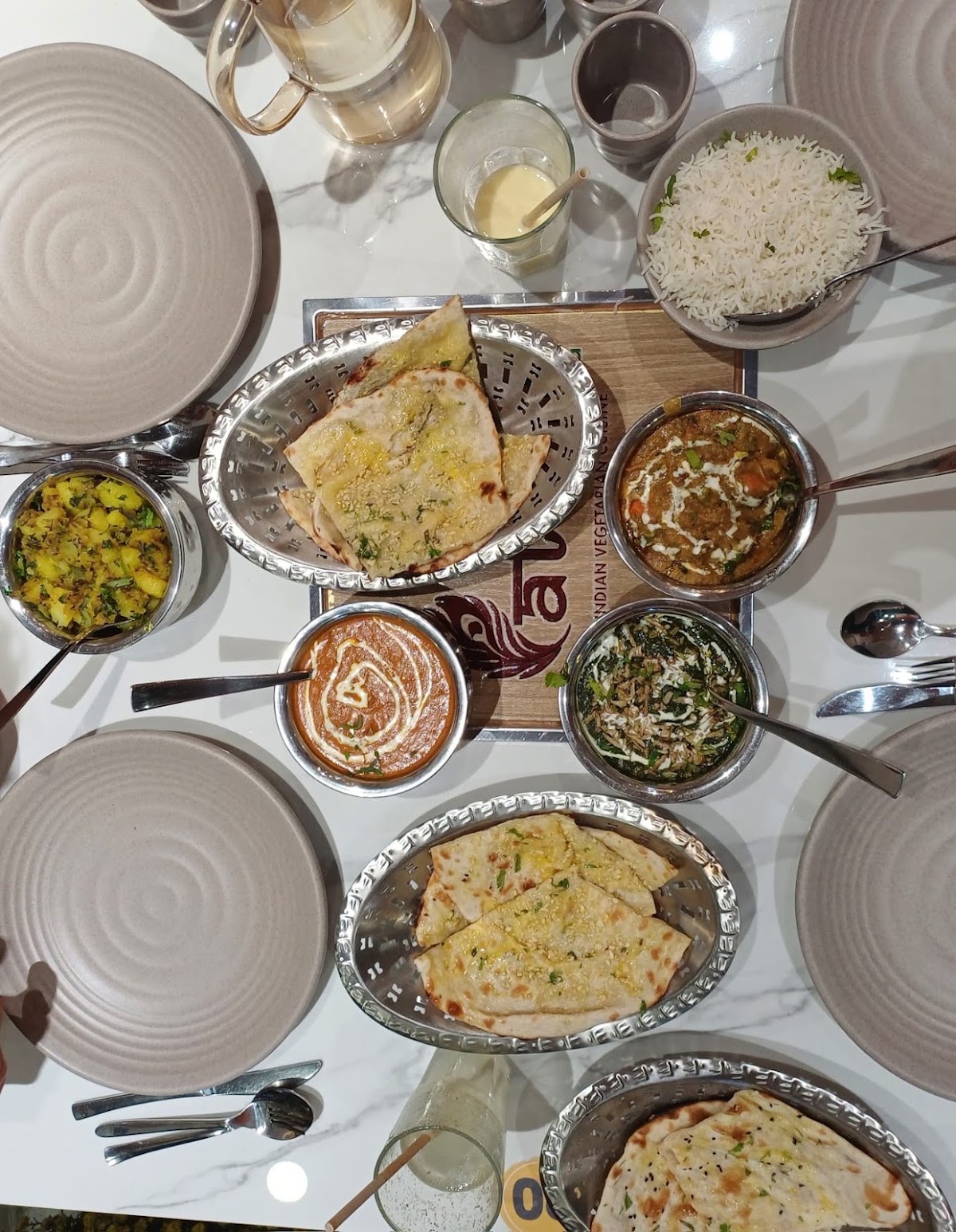 Overhead spread — naan baskets, curries, rice, chaas