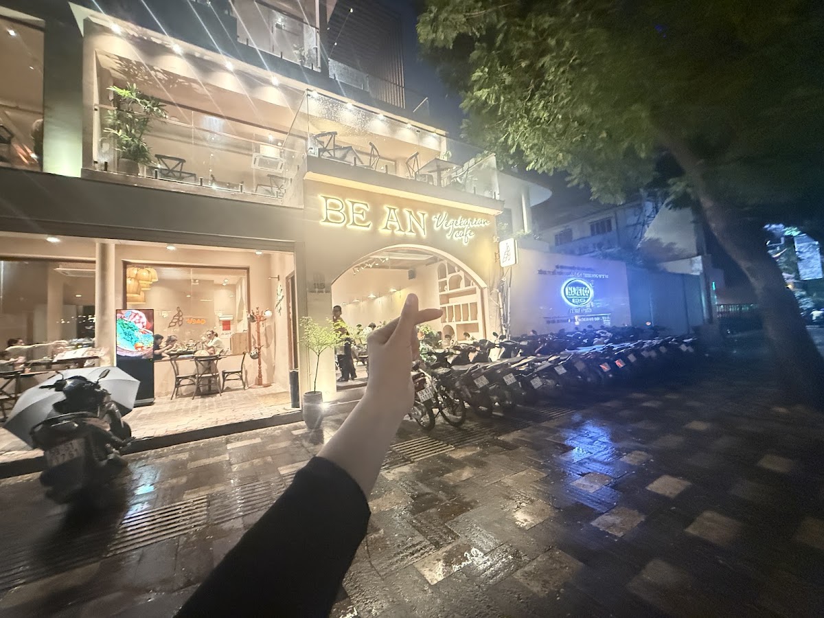 The facade at night from across the street — lit signage, diners inside, motorbikes, reflections on wet pavement