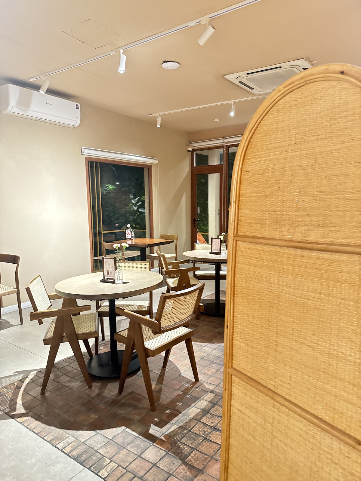 The side dining area — round tables, rattan chairs, curved woven rattan screen divider, brick-patterned floor tile