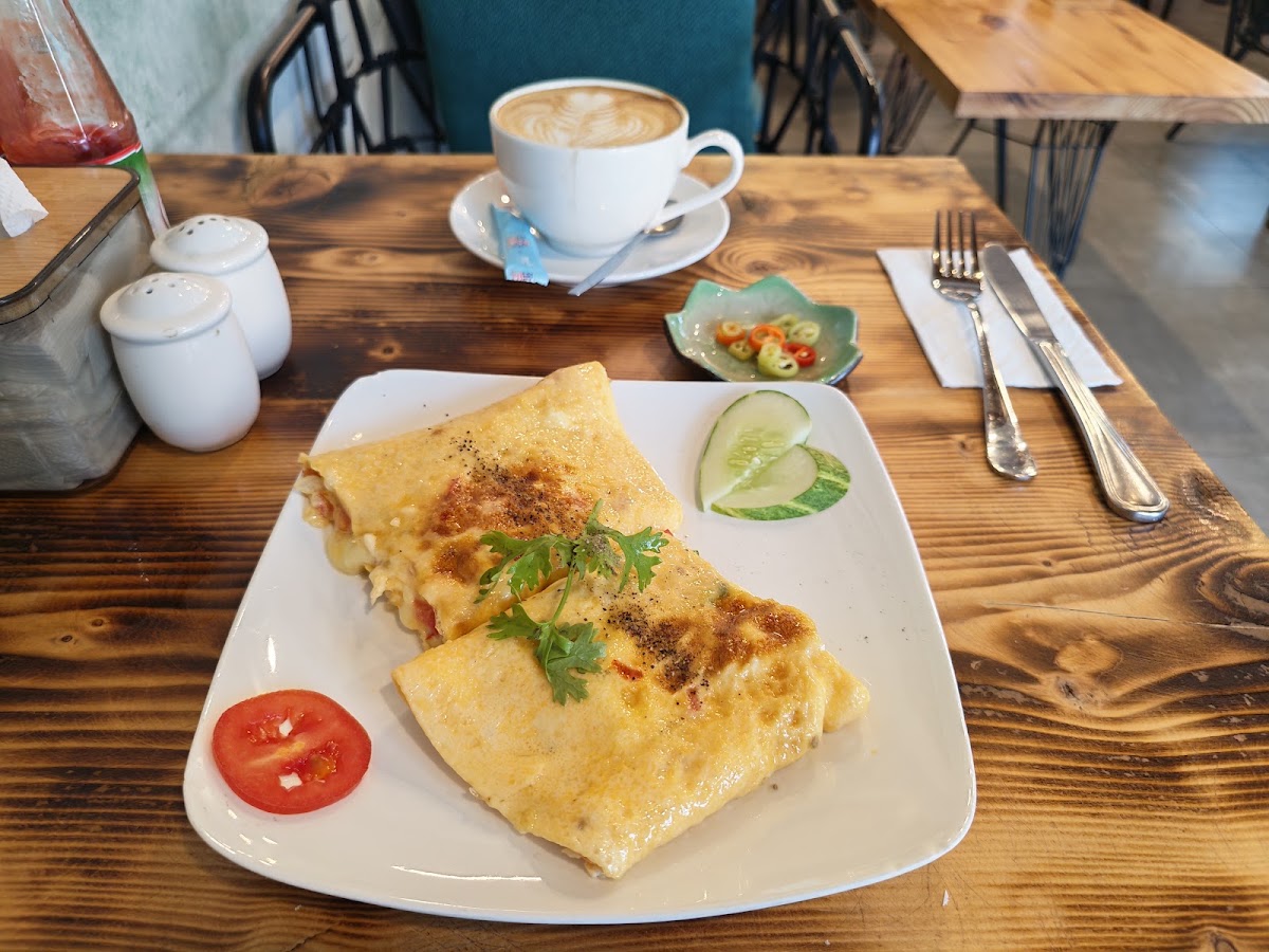 Dark wood table setting: omelet, latte-art cappuccino, white ceramic shakers
