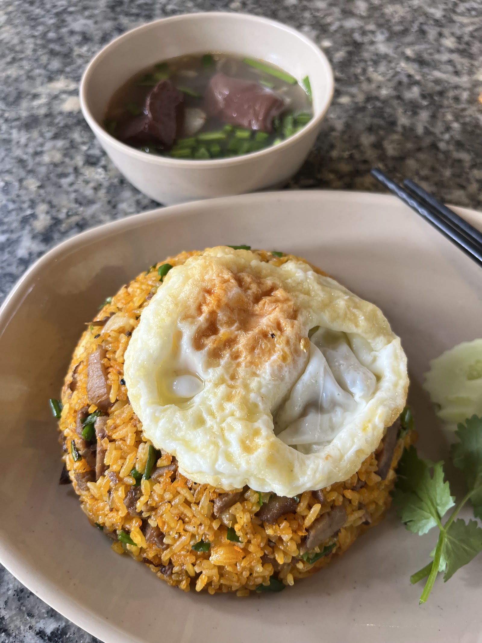 Goat fried rice topped with a fried egg, goat soup behind