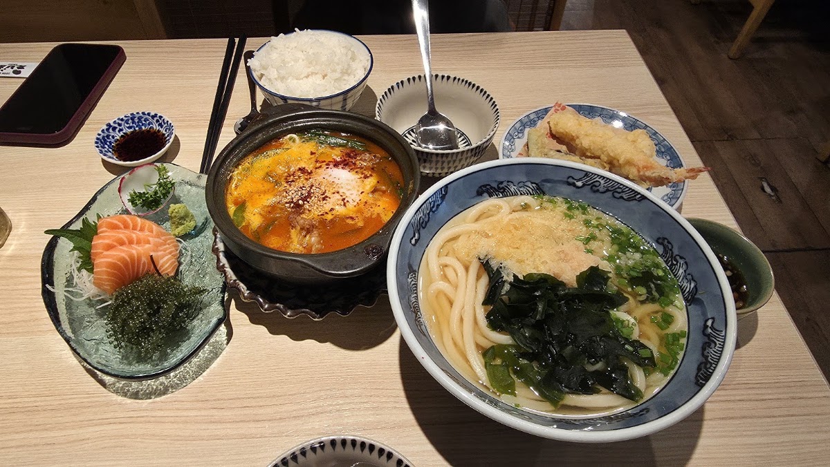 Mâm đồ ăn đầy đủ: tô udon, nồi đất, sashimi, tempura, cơm và chén chấm