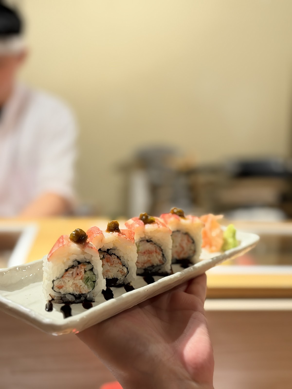 Uramaki cua cầm tay phủ trứng cá tobiko, nền quán ấm mờ phía sau