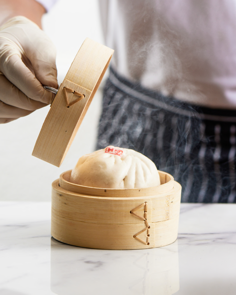 Steaming bao — a gloved hand lifts the bamboo steamer lid