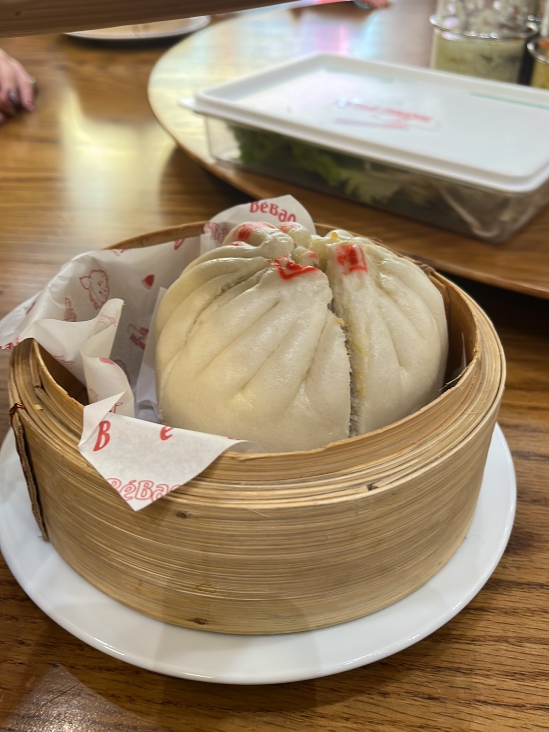 Steamed pork bun in a bamboo basket on branded paper