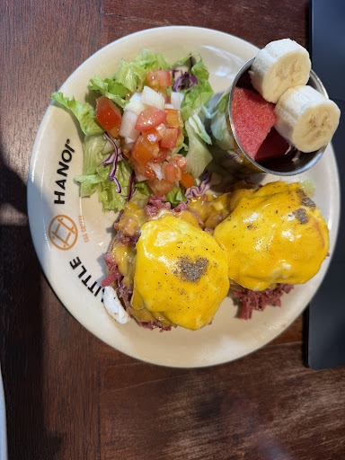 Eggs benedict with hollandaise, salad and fruit on a branded plate