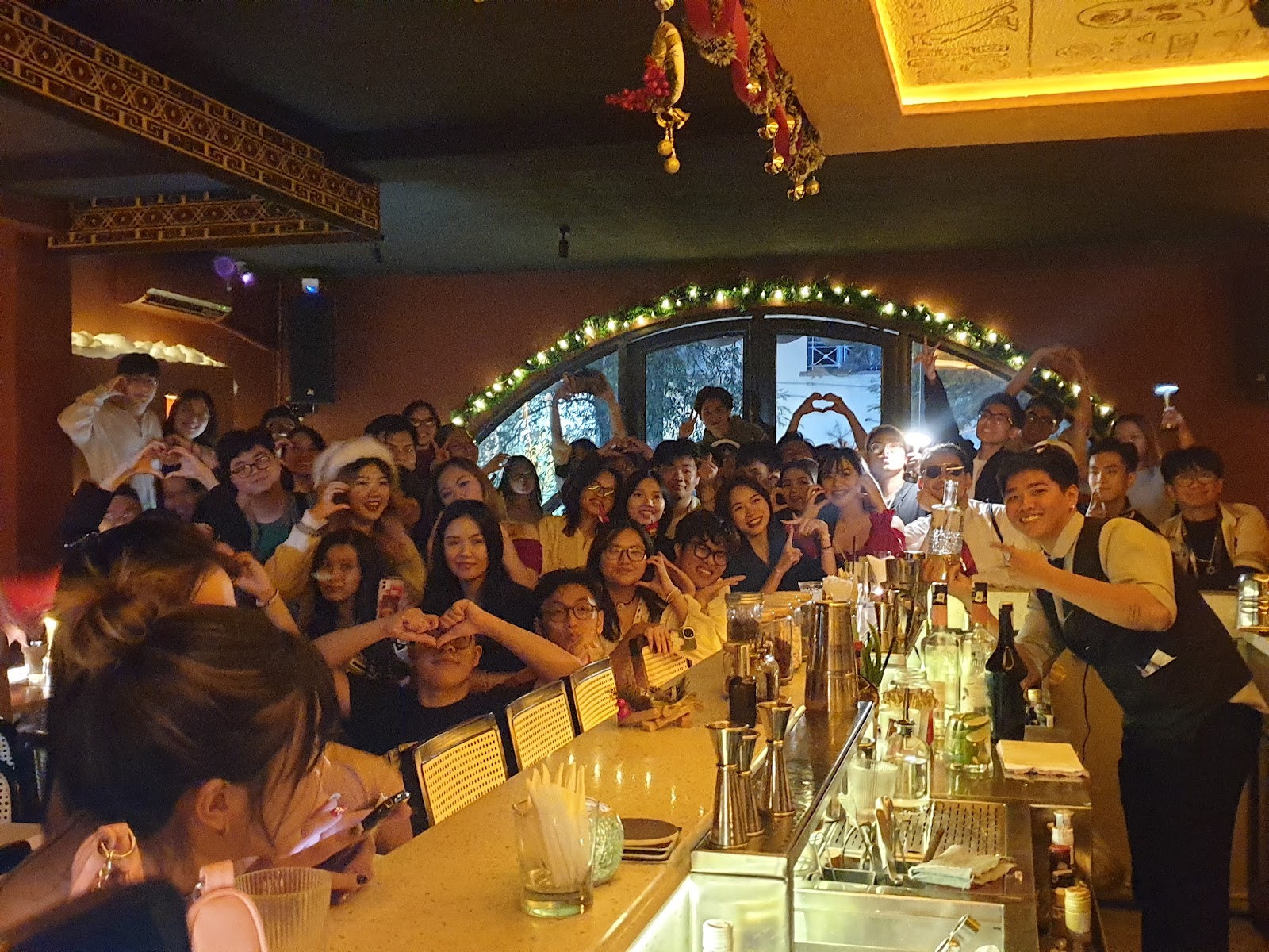Group celebration — young guests packed around the bar, fairy-lit arch window