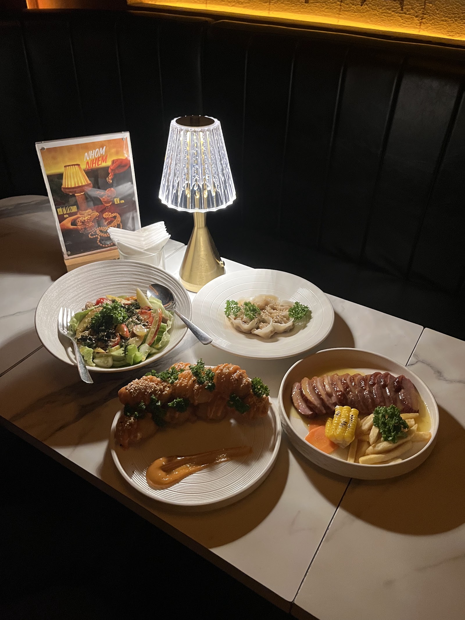 Table with salad, fried chicken bites, sliced beef, crystal table lamp in booth