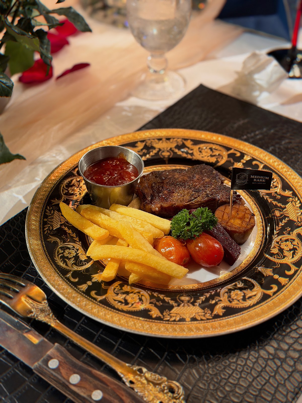 Steak with fries on a black-and-gold plate with a MEDIUM RARE flag and gold flatware
