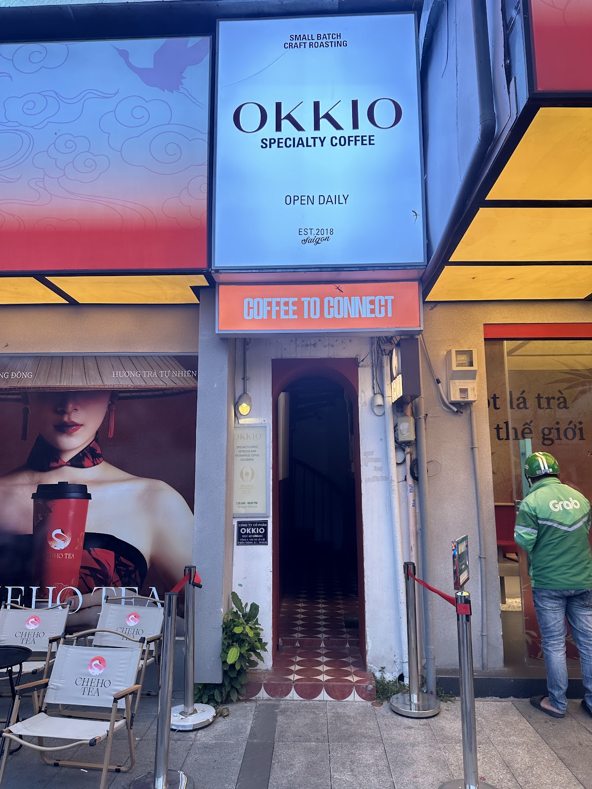 The storefront — backlit vertical OKKIO sign, orange COFFEE TO CONNECT sign, narrow arched doorway