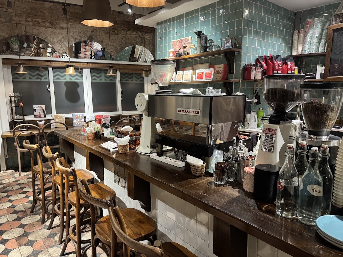 The coffee bar — La Marzocco machine, grinders, red coffee bags on open shelves, teal tile