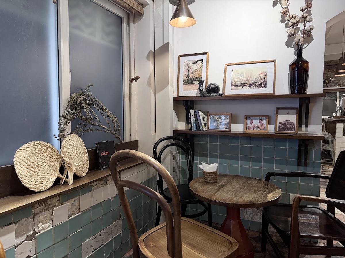 The quiet corner — round wooden table, bentwood chairs, rattan fans and dried botanicals on the sill, art shelves