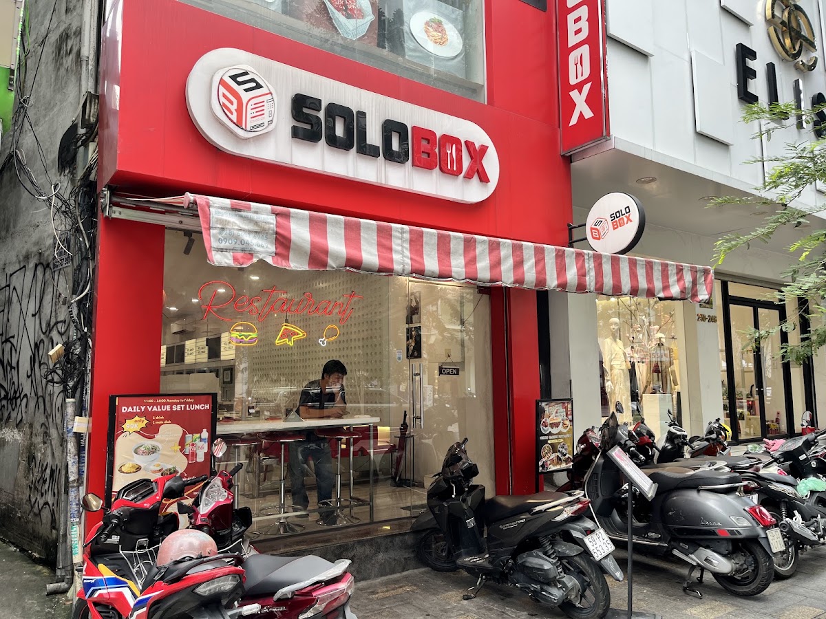 Red storefront — white oval SOLOBOX sign, SB monogram, red-and-white striped awning
