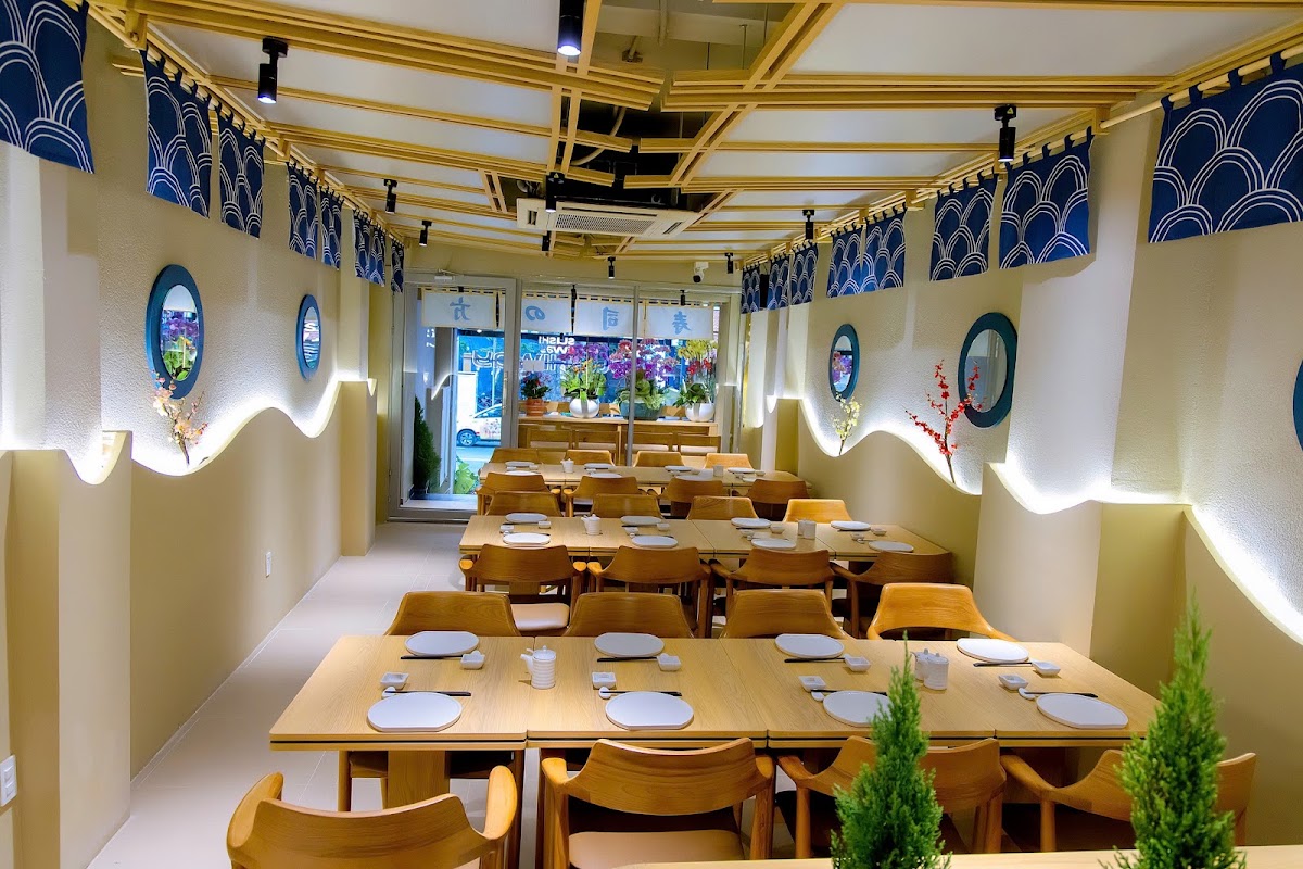 식당 홀 — 목재 슬랫 천장, 파란 물결 노렌, 물결 LED 코브, 현창 거울, 세팅된 목재 테이블, 문자 노렌의 유리 입구