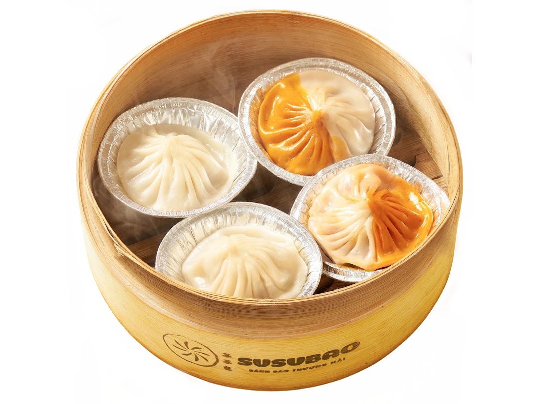 Soup dumplings in a SUSUBAO-branded bamboo steamer — white and orange wrappers, each in a foil cup