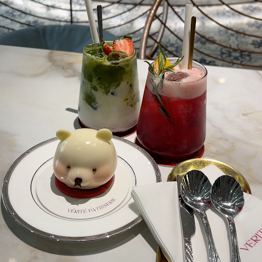 Bear-shaped white dessert on a branded VÉRITÉ plate with matcha + red berry drinks