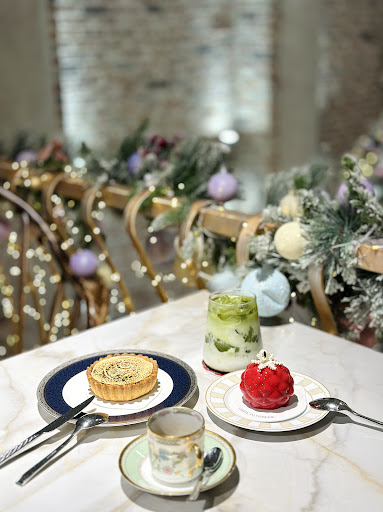 Marble-table setting: matcha tart, red raspberry-shaped cake, matcha drink + floral teacup, festive garland behind