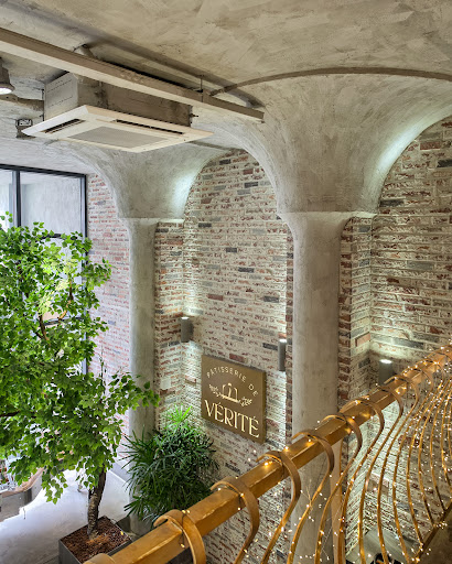 Mezzanine detail: exposed brick, curved coffered concrete ceiling, bamboo railing + fairy lights, indoor tree, brass sign